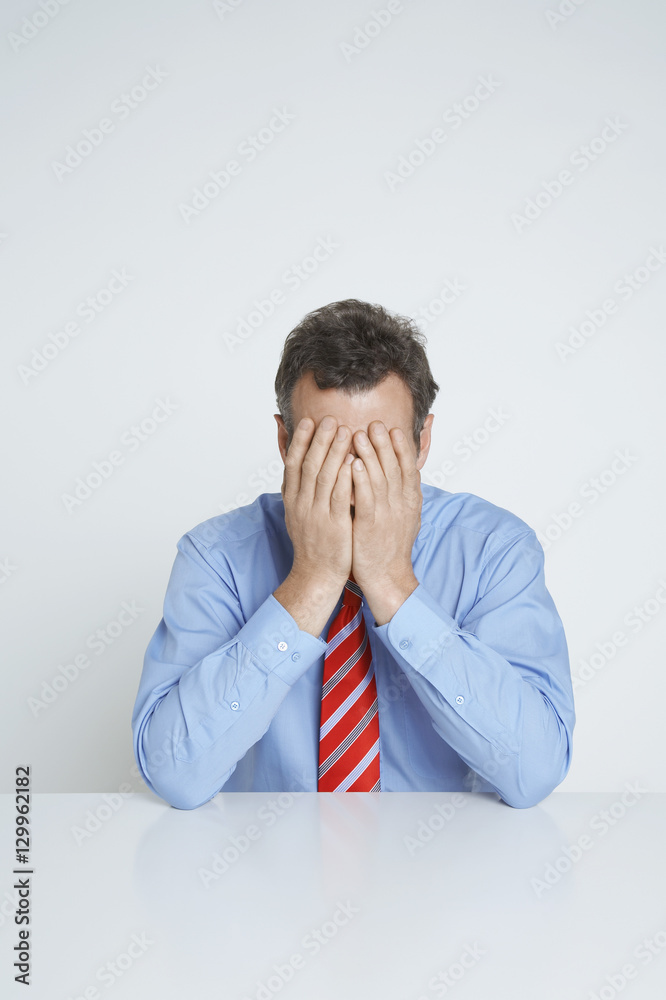 Depressed businessman covering face with hands at desk isolated over white background Depressed businessman covering face with hands at desk isolated over white background