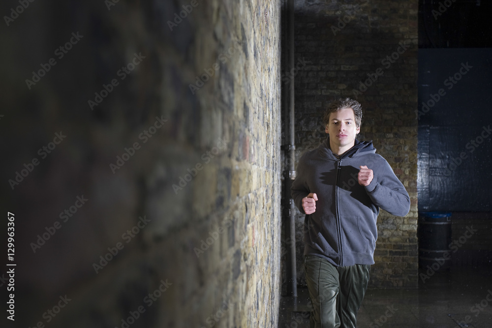 Portrait of a young man jogging besides brick wall at night
