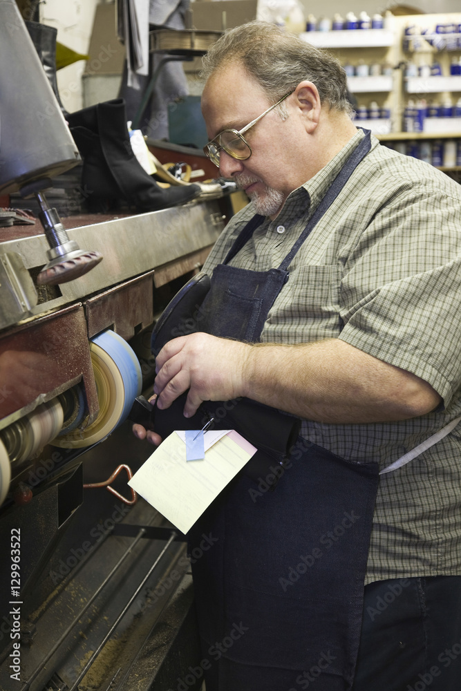 Obraz premium Side view of a male shoemaker at work in traditional workshop