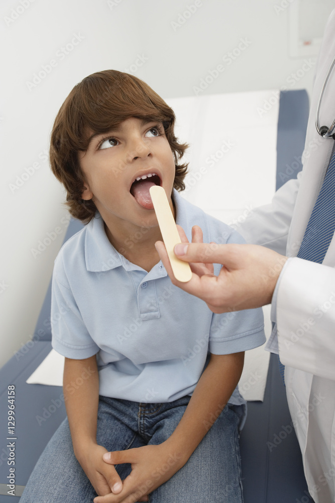 Doctor examining boy's throat with tongue depressor in clinic Stock