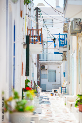 Fototapeta Naklejka Na Ścianę i Meble -  The narrow streets of greek island with blue balconies, stairs and flowers. Beautiful architecture building exterior with cycladic style.