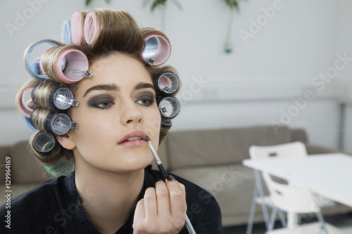 Closeup of a female model in hair curlers applying lip gloss