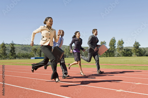 Four multiethnic business people running together on racing track