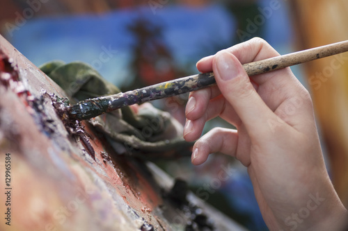 Closeup of a woman's hand mixing colours on art palette with paintbrush