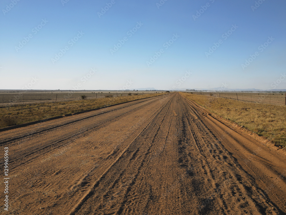 Country view of a long and straight dirt road leading into the distant horizon Country view of a long and straight dirt road leading into the distant horizon