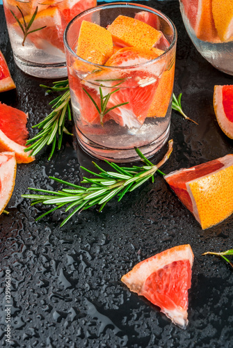 Refreshing summer detox cocktail of grapefruit and rosemary, with Ingredients, on black background, close view
