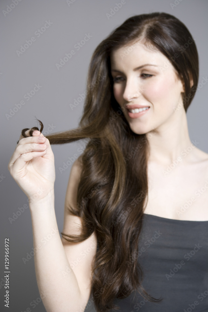 Closeup of a beautiful young woman twisting long brown hair against gray background Closeup of a beautiful young woman twisting long brown hair against gray background