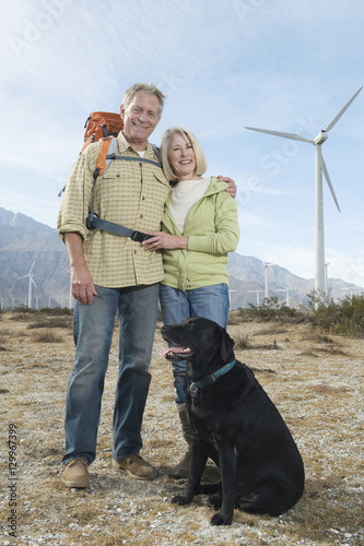 Portrait of a lovely Caucasian senior couple with dog near wind farm
