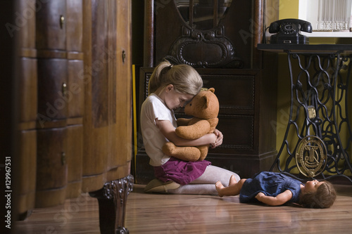 Side view of a little girl embracing teddy bear on floor in home