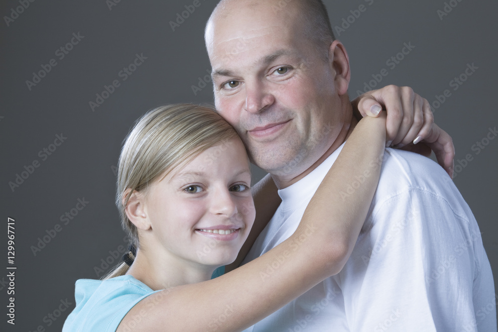 Young daughter embracing her father against gray background Young daughter embracing her father against gray background