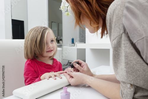 Woman applying nail polish on little girl's hand