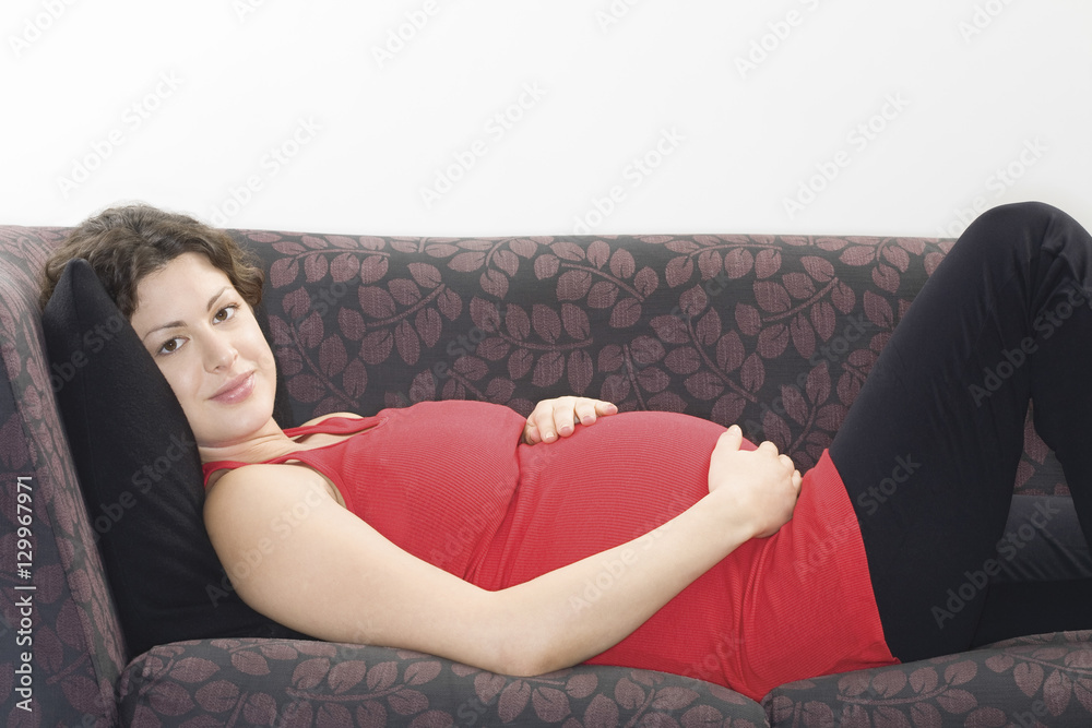 Side view portrait of a smiling young pregnant woman relaxing on sofa Side view portrait of a smiling young pregnant woman relaxing on sofa