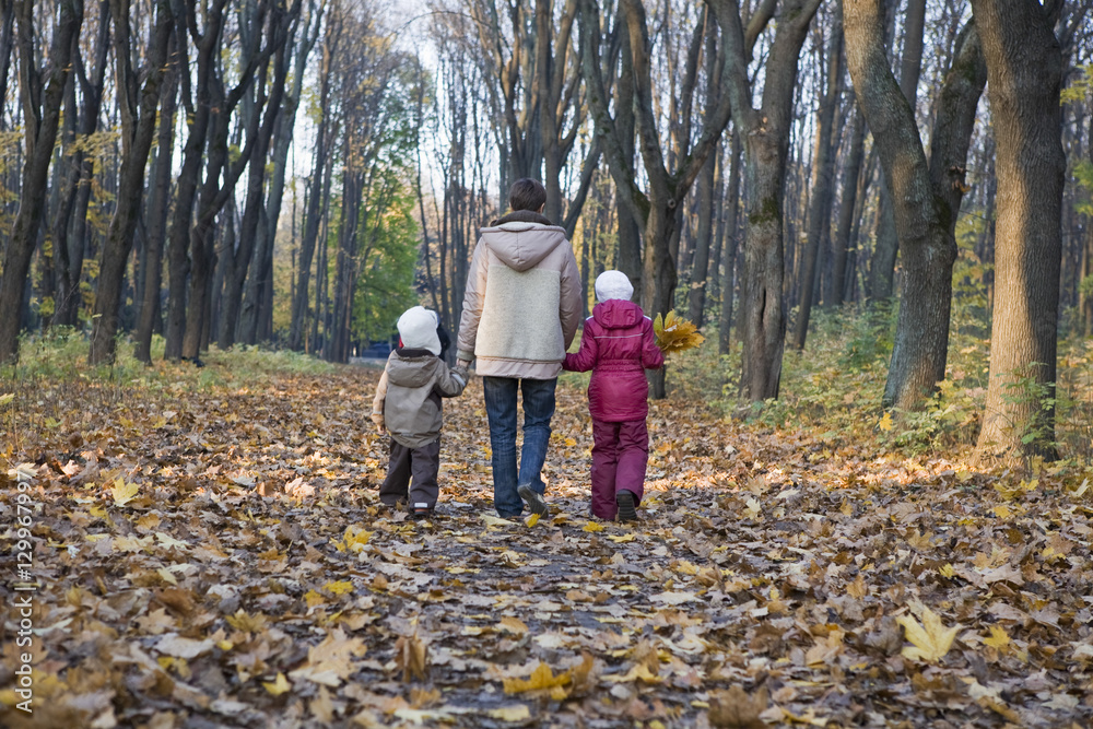 Fototapeta premium Full length rear view of mother and children walking in the park