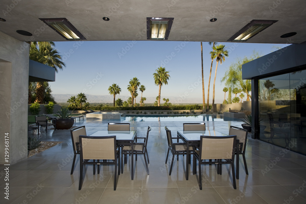 Outdoor tables on patio against swimming pool and sky