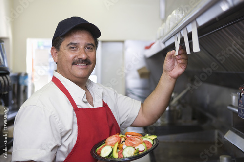 Portrait of Hispanic Latin man with served food standing in restaurant kitchen