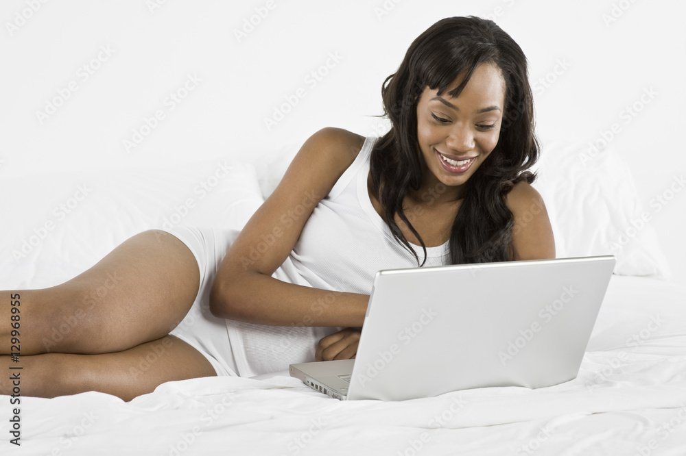 Smiling young African American woman using laptop in bed Smiling young African American woman using laptop in bed