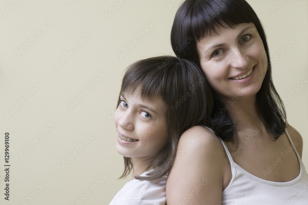 Portrait of a mother and daughter smiling against colored background