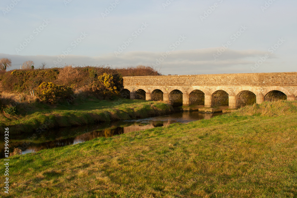 The warm glow of soft December sunlight brings out the texture of the stones in this 12 arches bridge at Murlough, Dundrum in County Down, Northern Ireland