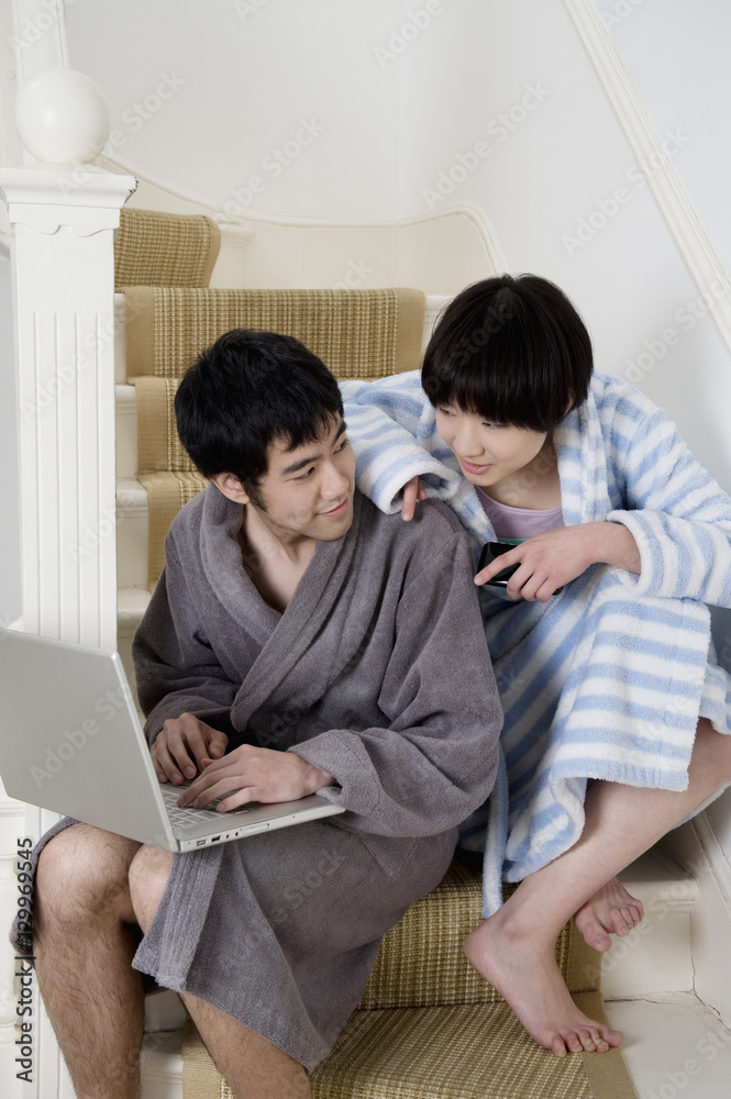 Young couple in bathrobe sitting on stairway with laptop Young couple in bathrobe sitting on stairway with laptop