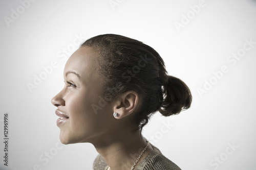 Side view of a smiling young woman looking up against gray background