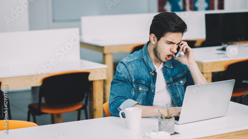 Young busy man with beard working on laptop and using mobile phone