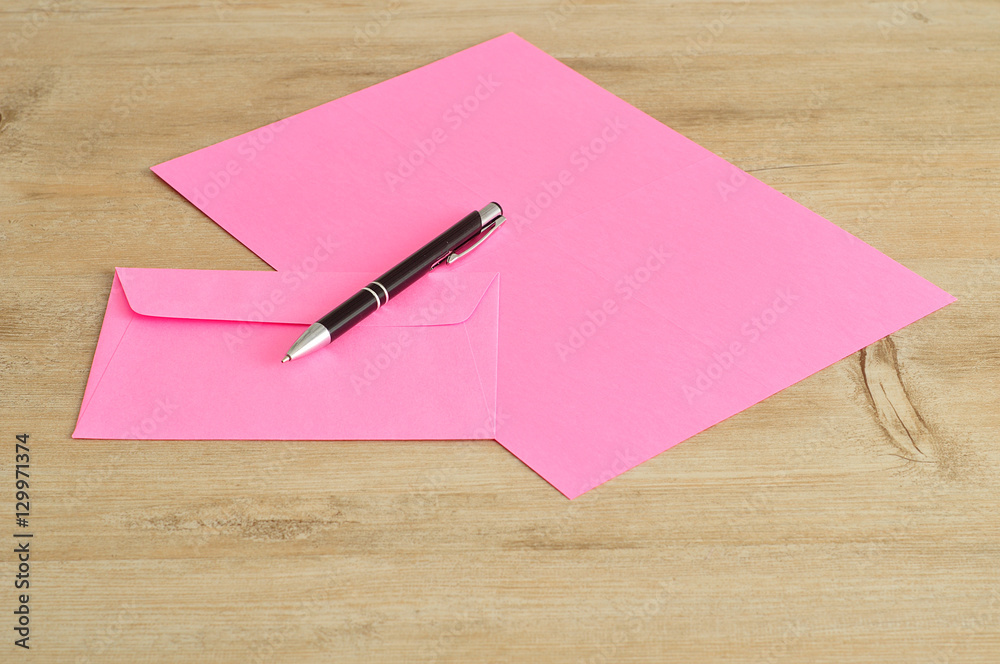 A pink paper and envelope with a  pen