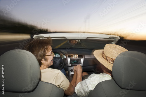 Rear view of senior couple driving in convertible on country road at dusk