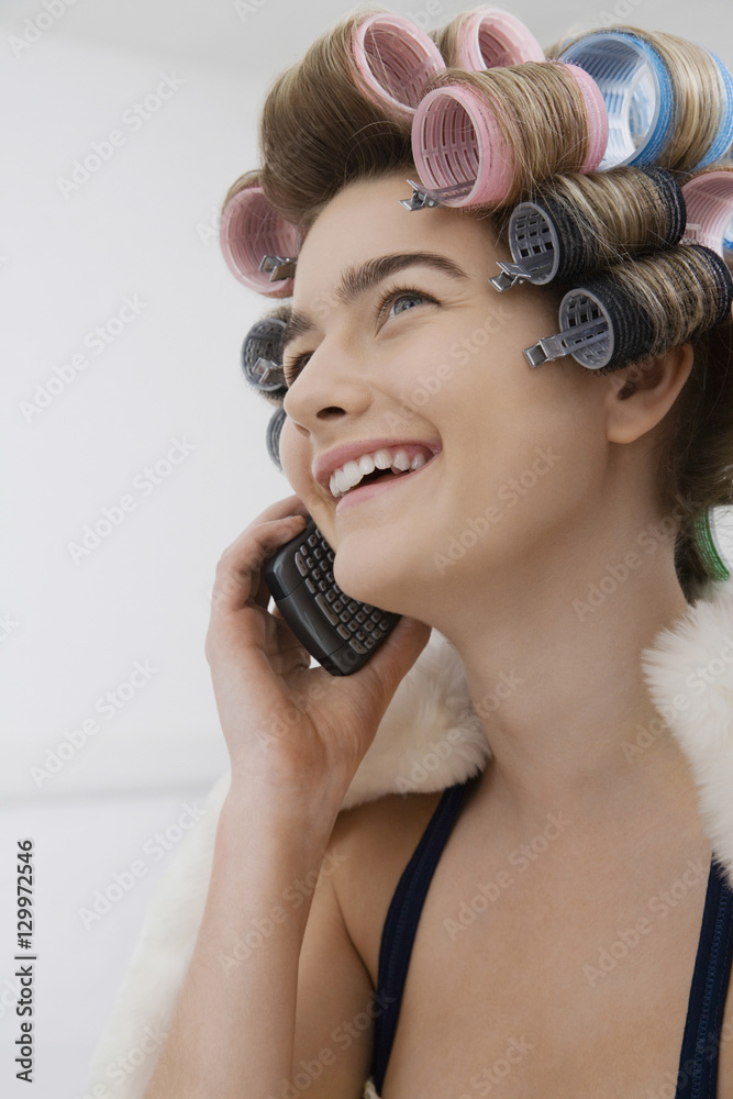 Fototapeta premium Closeup of a cheerful female model in curlers talking on cellphone