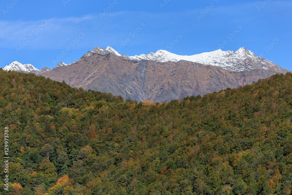 Beautiful scenic colorful autumn landscape of the Main Caucasus ridge with snowy mountain peak tops on blue sky background
