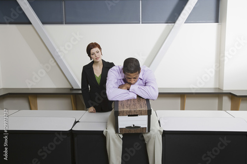 Woman looking at depressed African American man sit on desk with moving box