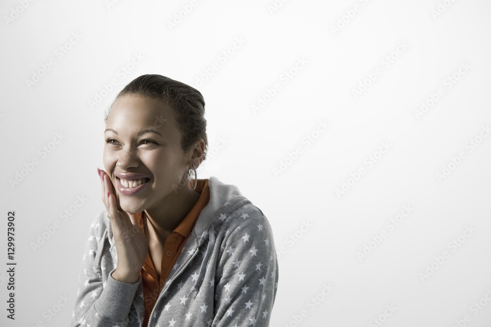 Smiling young woman touching her cheek against gray background Smiling young woman touching her cheek against gray background