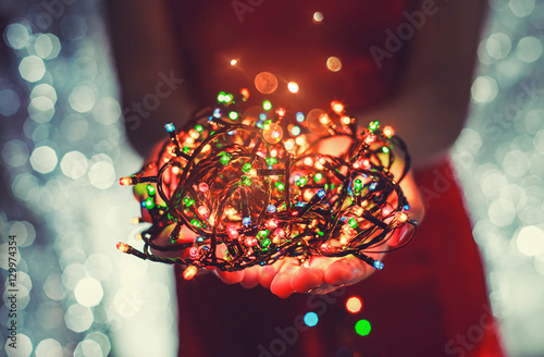 Female hands holding Multicolored Christmas light decorations on dark holiday background. Xmas and New Year theme. Toning