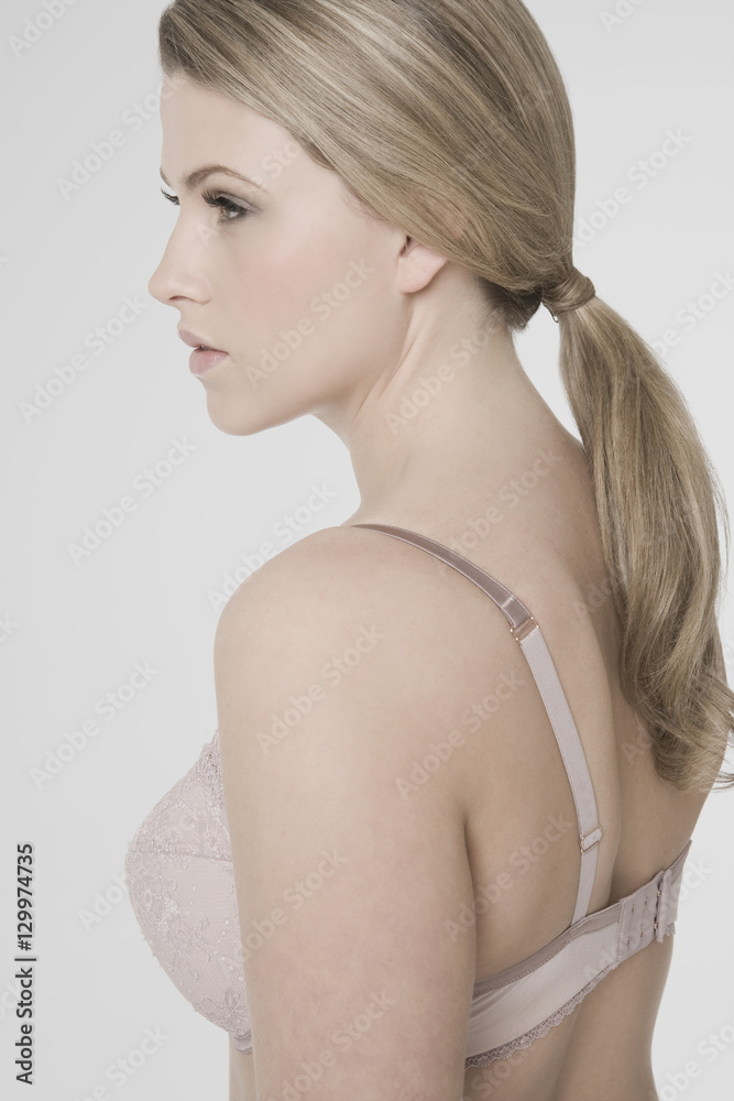 Closeup side view of a sexy young woman in bra against gray background
