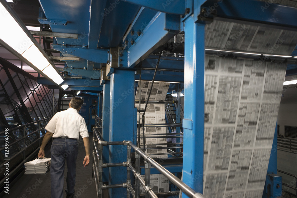 Rear view of a man carrying stack of newspapers in the factory