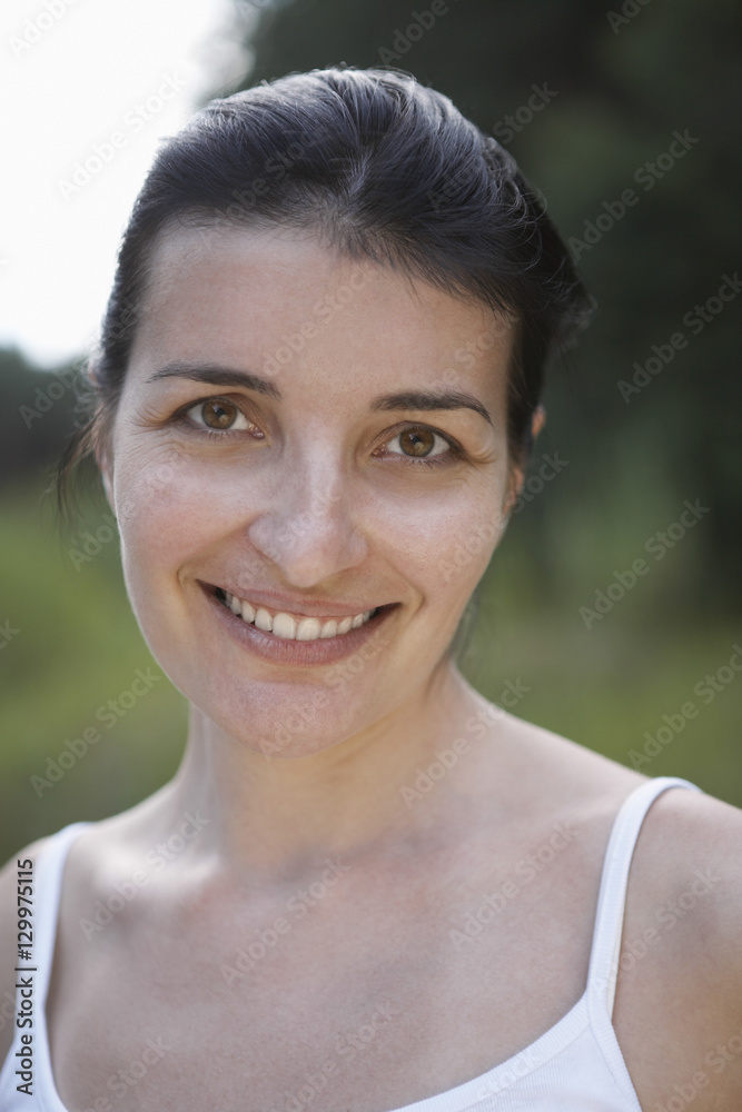 Closeup portrait of a smiling woman in tank top against blurred plants Closeup portrait of a smiling woman in tank top against blurred plants