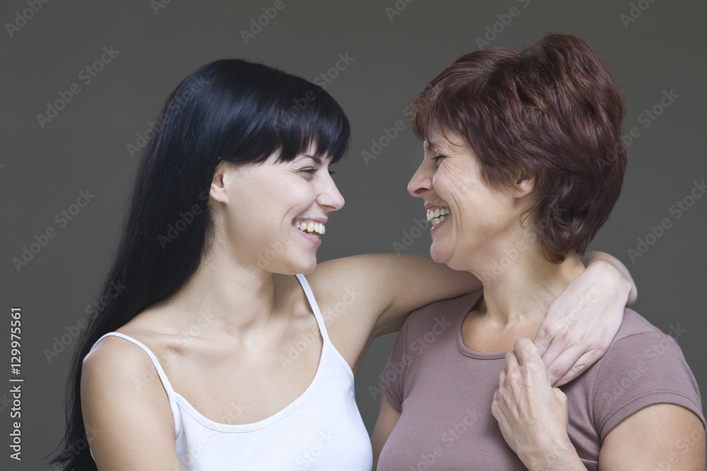 Closeup of a smiling young woman embracing her mother against gray background Closeup of a smiling young woman embracing her mother against gray background