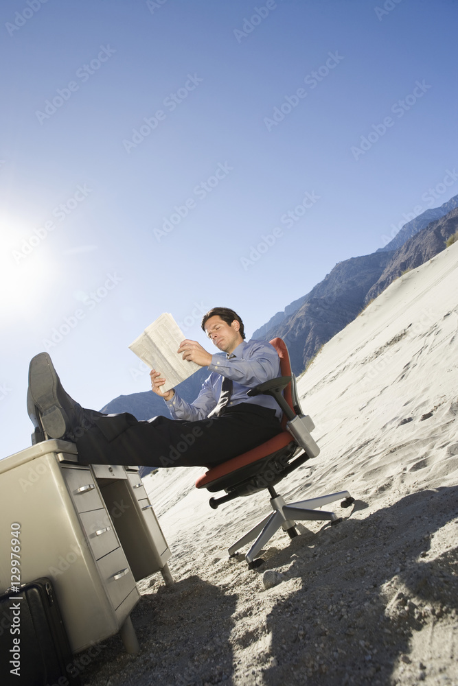 Businessman reading document with legs on desk in desert