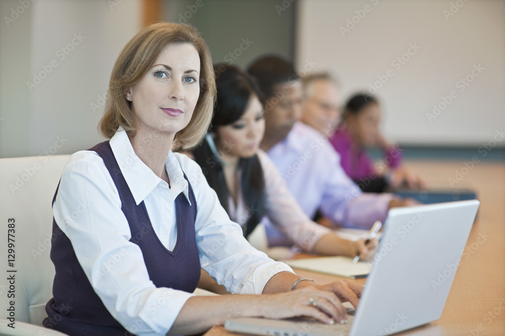 Portrait of a confident businesswoman with laptop and multiethnic colleagues in conference room