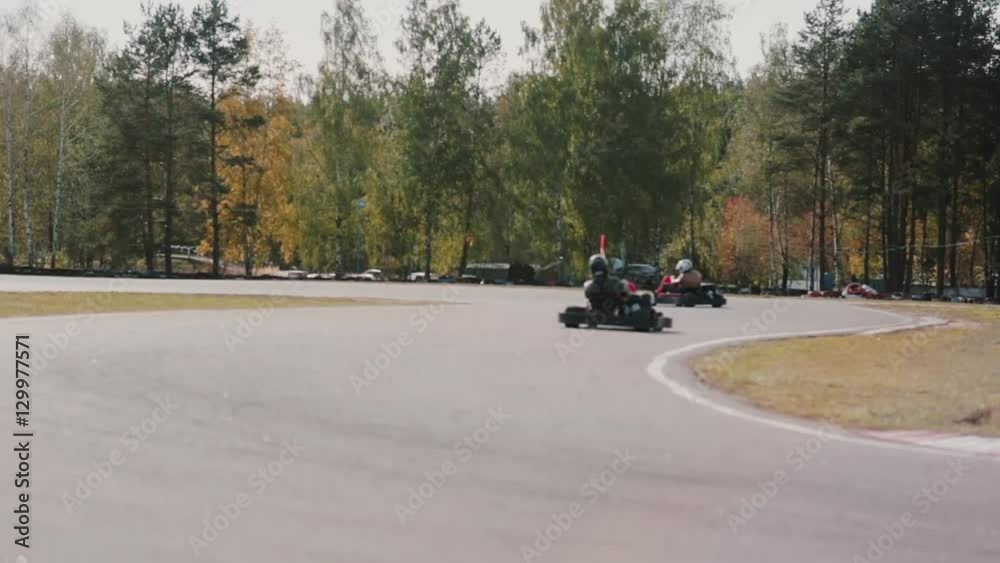 Two drivers on a go-kart track pass by the camera. Go-kart race.