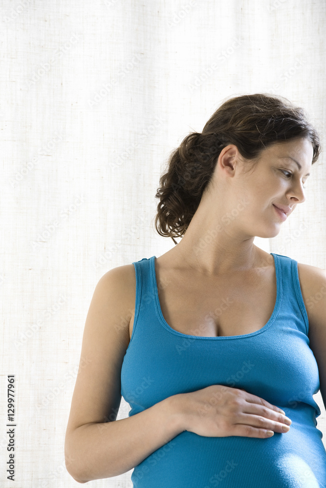 Thoughtful pregnant woman touching stomach against white background Thoughtful pregnant woman touching stomach against white background