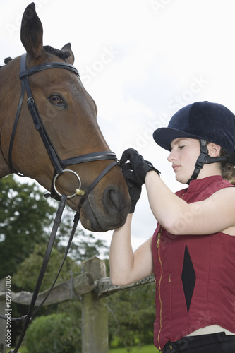 Side view of a young woman tightening horse's bridle outdoors
