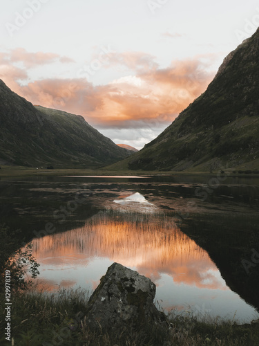 Sunset in the mountains at a calm lake reflecting the red and orange sky symmetrically and mirror like