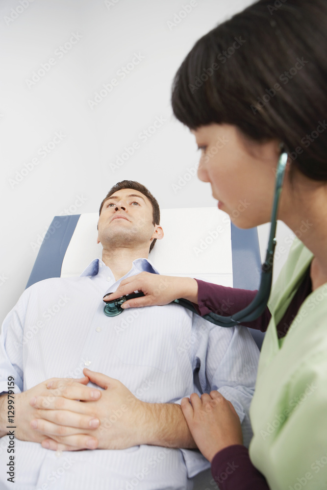 Fototapeta premium Female doctor examining a male patient with stethoscope in the clinic