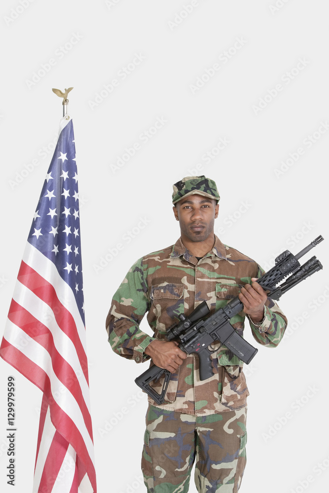Portrait of US Marine Corps soldier with M4 assault rifle standing by American flag over gray background Portrait of US Marine Corps soldier with M4 assault rifle standing by American flag over gray background