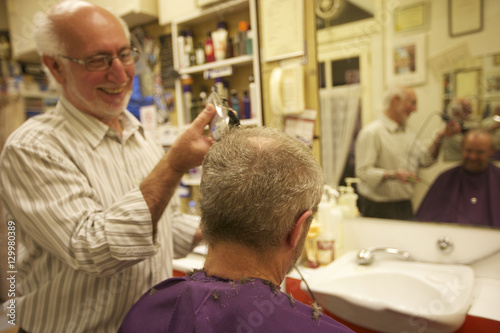 Happy man cutting senior customer's hair with razor