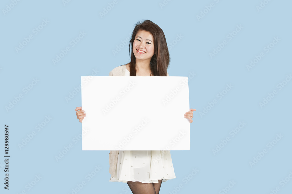Portrait of a beautiful young woman holding blank cardboard over blue background Portrait of a beautiful young woman holding blank cardboard over blue background