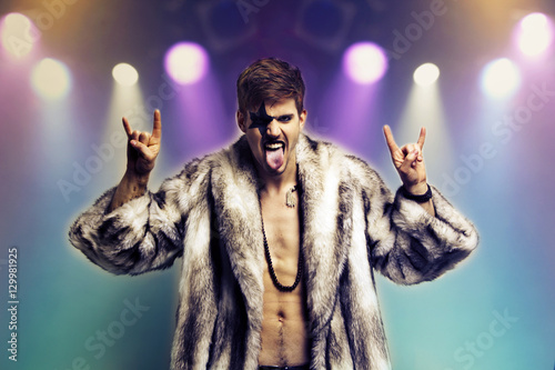 Εκτύπωση καμβά Portrait of young man in fur coat making rebellious hand gestures in rock concer