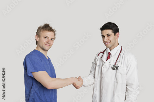 Portrait of doctor and male nurse shaking hands over gray background