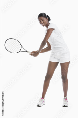 Portrait of young woman with tennis racket standing over white background