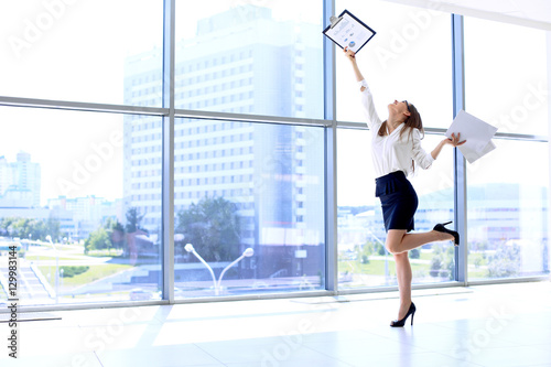 Happy modern business woman with financial report is running in office hall
